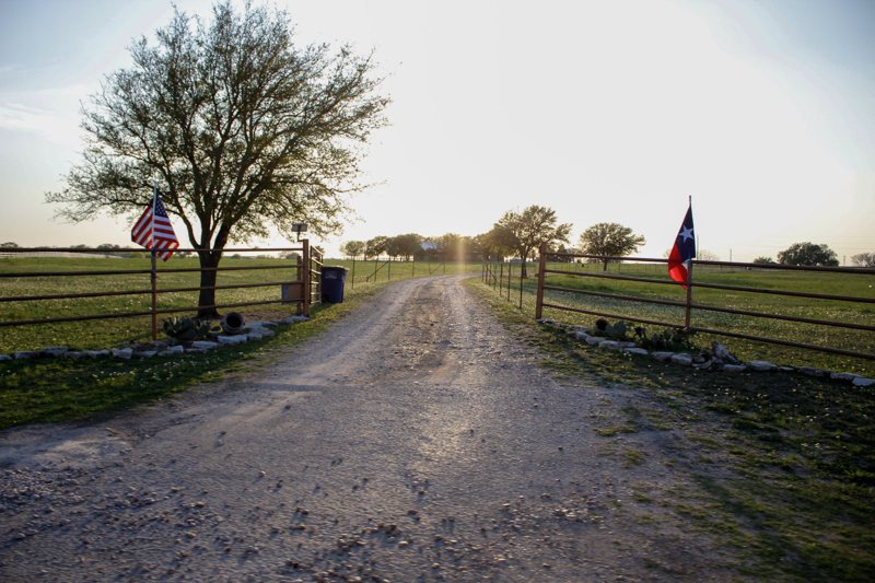 A Texas ranch road under the US and Texas flags.
