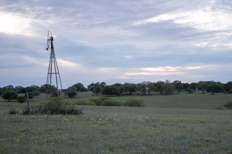 Windmill on open ranchland under cloudy sky