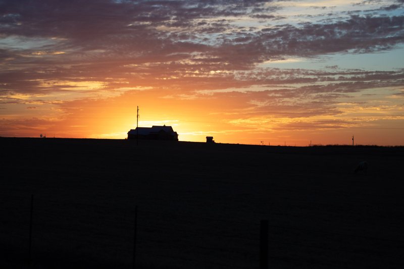 Ranch house silhouetted against a blazing orange sunset