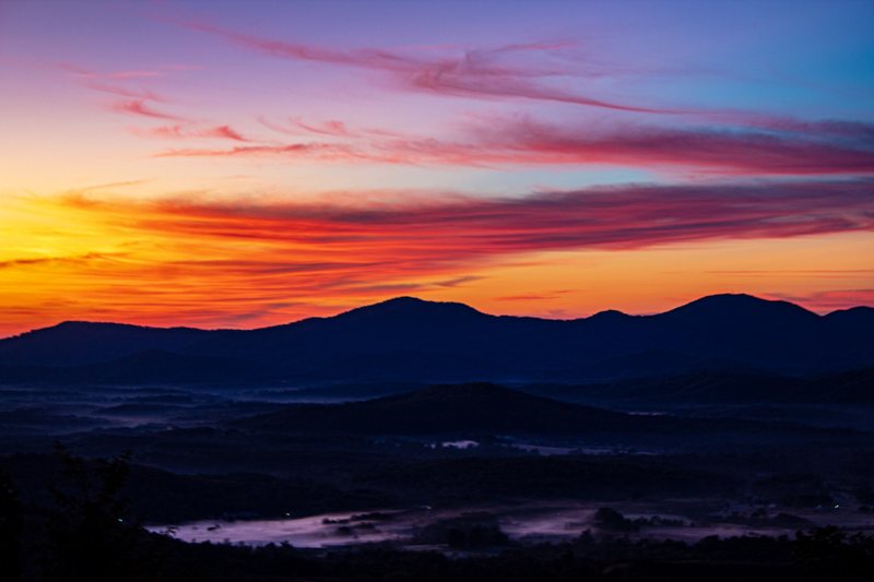 Magenta and orange sunrise over layered blue mountains with valley fog