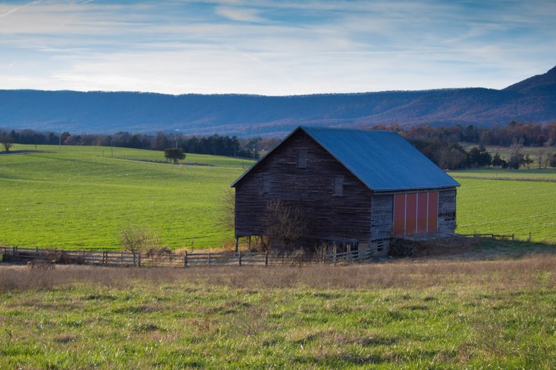 Blue-roofed barn in green pasture with mountains